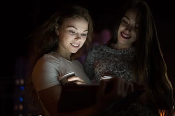 Two woman friends look down on digital tablet in balcony at night — Stock Photo, Image