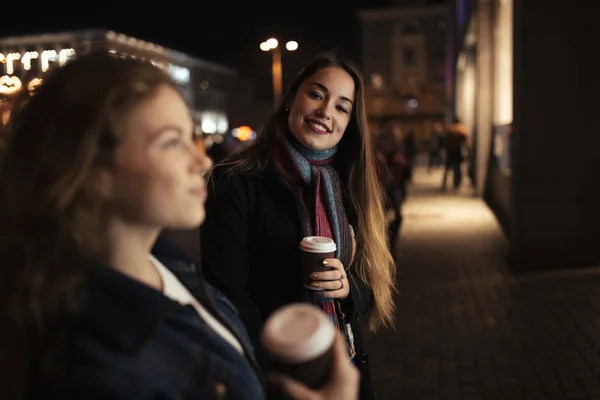 Dos amigas caminando por la calle de la ciudad por la noche y tomando café — Foto de Stock