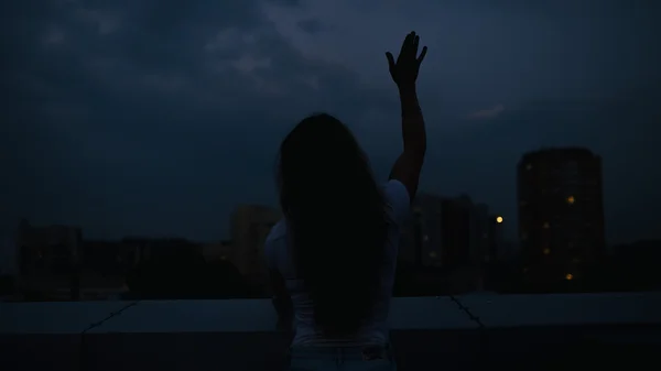 Silhouet van de vrouw een hand omhoog gebaar maken in schemering stad — Stockfoto