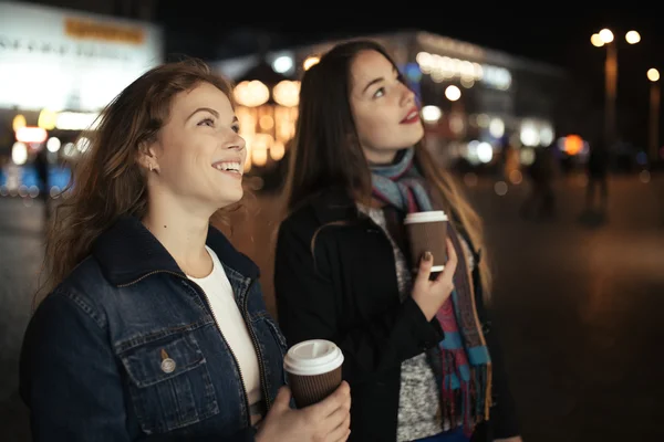 Dos amigas caminando por la calle de la ciudad por la noche y tomando café — Foto de Stock