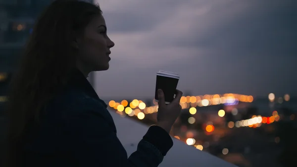 Woman enjoying coffee looking to evening city — Stock Photo, Image
