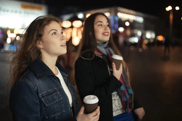 Dos amigas caminando por la calle de la ciudad y tomando café por la noche —  Fotos de Stock