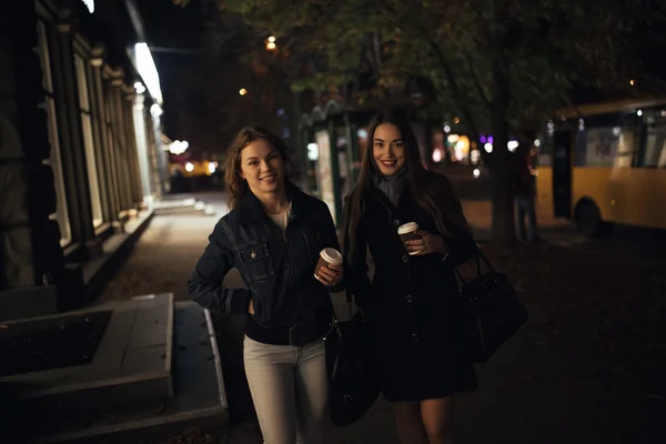 Duas amigas na moda que andam na avenida de cidade à noite — Fotografia de Stock