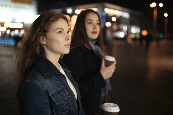 เพื่อนผู้หญิงสองคนเดินบนถนนในเมืองและดื่มกาแฟตอนกลางคืน — ภาพถ่ายสต็อก