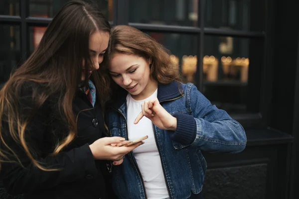 Outdoors portrait of two women drinking coffee and looking at smartphone in city — Stock Photo, Image