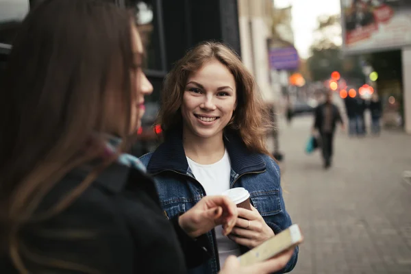 Outdoors portrait of two women drinking coffee and looking at smartphone in city — Stock Photo, Image