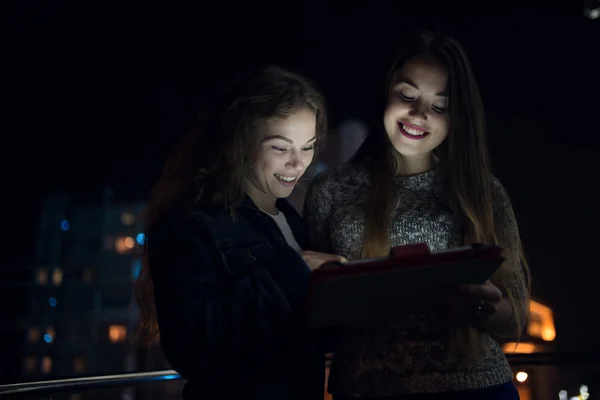 Two women look down to digital tablet in balcony at night — Stock Photo, Image