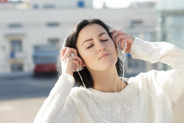 Woman in white earphones enjoying to listen music in city