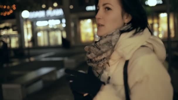 Mujer caminando en la ciudad por la noche y hablando en cámara — Vídeos de Stock