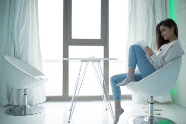 Kadın rahat ev koltuğa oturan ve kullanarak tablet Pc