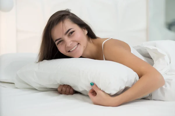 Kobieta leżąc na białe łóżko w domu i uśmiech. Dzień dobry. — Zdjęcie stockowe