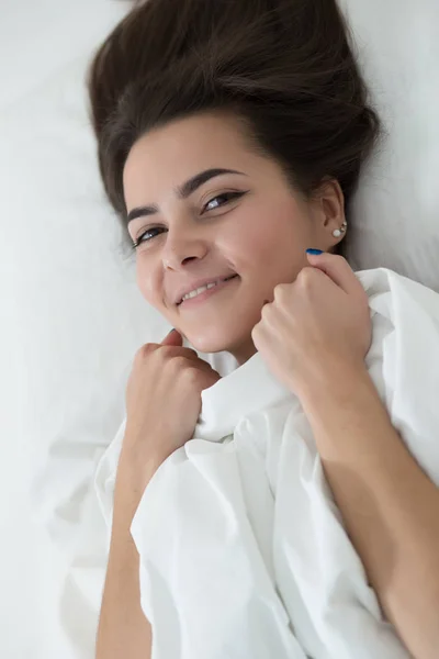 Женщина лежит на белой кровати дома и улыбается. Доброе утро. . — стоковое фото