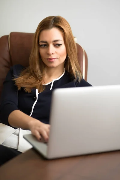 Mujer sentada en su lugar de trabajo en la oficina y trabajando por cuaderno —  Fotos de Stock