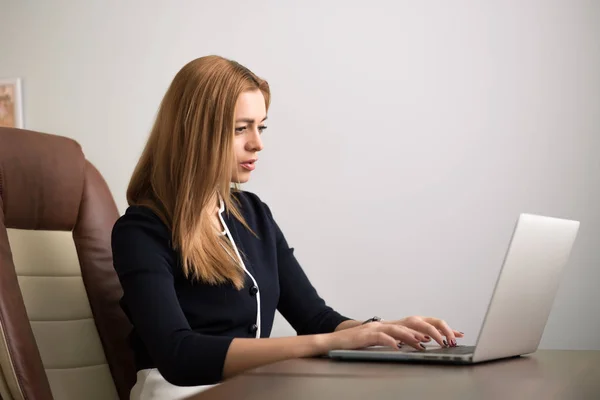 Mujer sentada en su lugar de trabajo en la oficina y trabajando por cuaderno —  Fotos de Stock