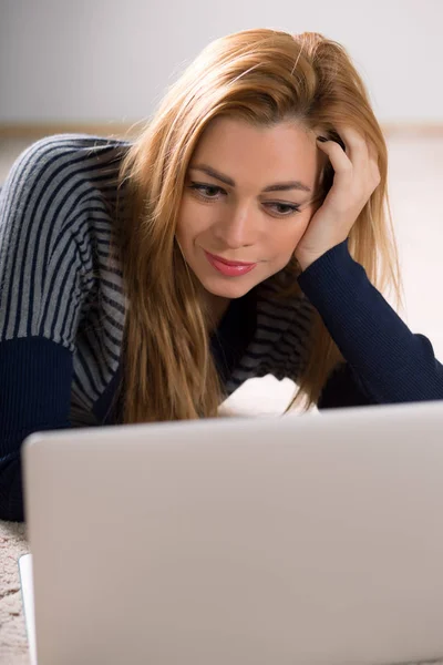 Beautiful adult woman lying on floor at home and using laptop — Stock Photo, Image