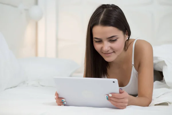 Современная женщина лежит в белой кровати со своим планшетным компьютером — стоковое фото