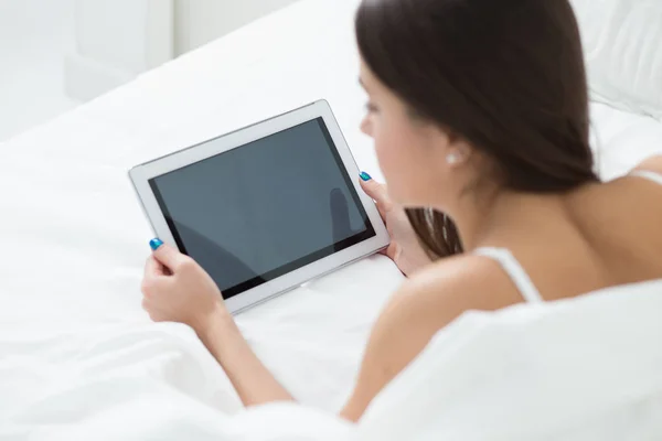 Frau liegt mit Tablet-PC im Bett und surft im Internet — Stockfoto