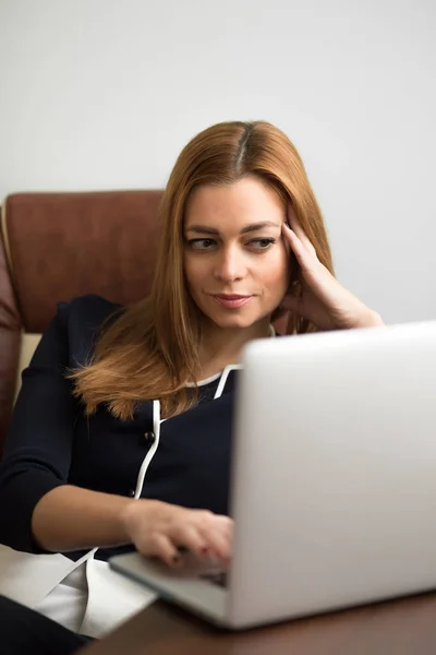 Женщина сидит на своем рабочем месте в офисе и работает за ноутбуком — стоковое фото