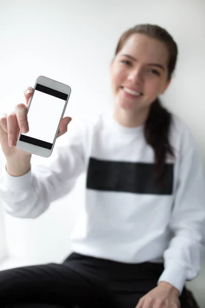 Nuori nainen näyttää näytön älypuhelimellaan valkoista taustaa vasten — kuvapankkivalokuva