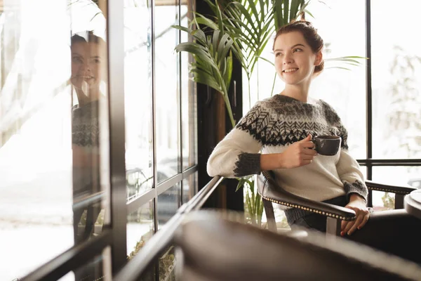 Vrouw in pullover met kopje koffie in een café zitten en glimlachen — Stockfoto