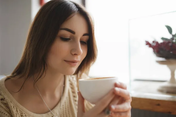 Женщина печатает текст на смартфоне в кафе, пока кофе охлаждается — стоковое фото