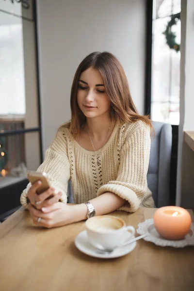 Kvinne skriver tekst på smarttelefon på kafe mens kaffe er kjølig – stockfoto