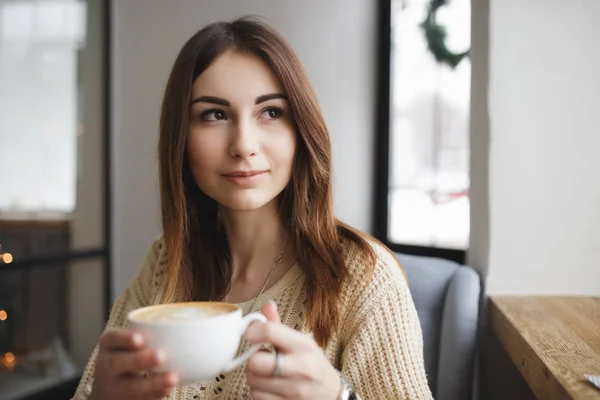 Mujer sentada con una taza de café en un café y mirando a la ventana — Foto de Stock