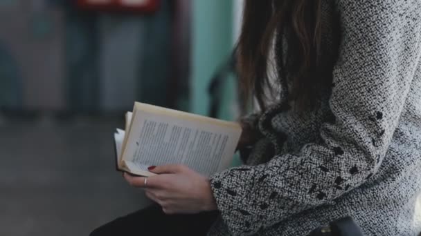 Женщина, читающая книгу в старом общественном здании, сидит на подоконнике — стоковое видео