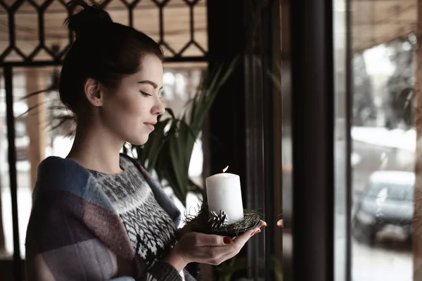 Taidekuva - nainen pitelee palavaa kynttilää kahvilan ikkunassa — kuvapankkivalokuva