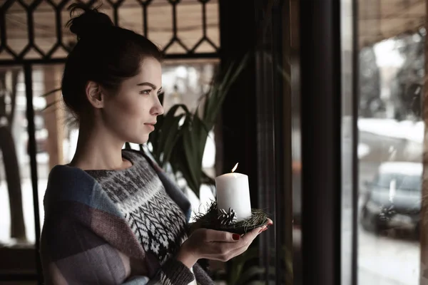 Художественное фото - женщина, держащая горящую свечу у окна в кафе — стоковое фото