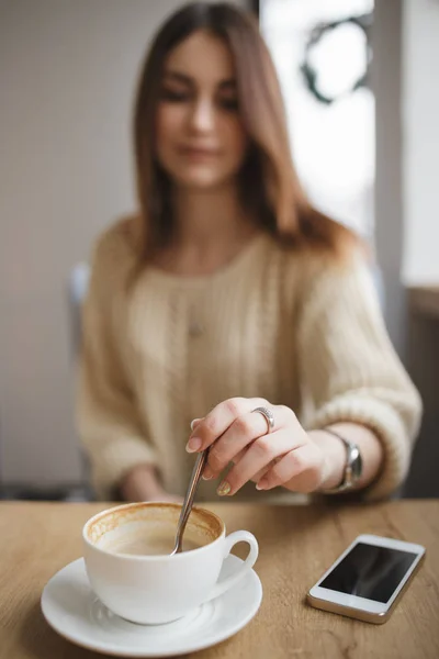 Kvinne rører sukkerskje i en kopp cappuccino på kafe – stockfoto