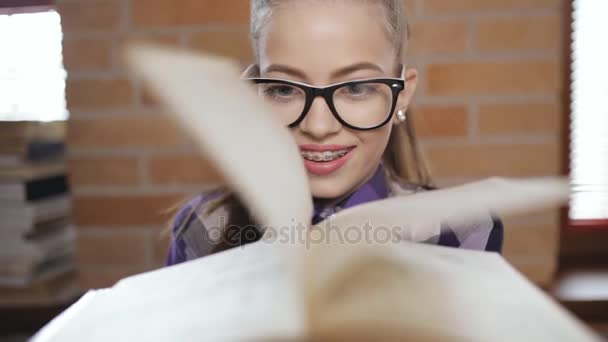 Tiener meisje portret. Leerling in brillen spelen met pagina's van het boek. — Stockvideo