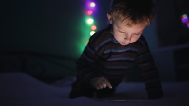 Menino brincando com tablet pc ou smartphone na cama à noite — Vídeo de Stock