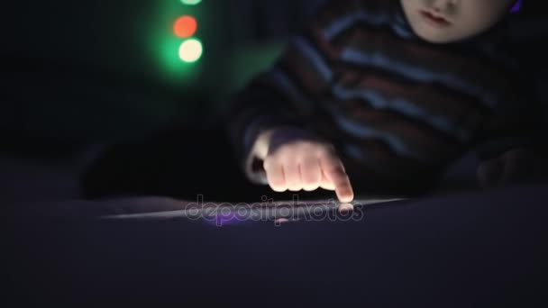 Маленький хлопчик грає з планшетним ПК або смартфоном на ліжку вночі — стокове відео