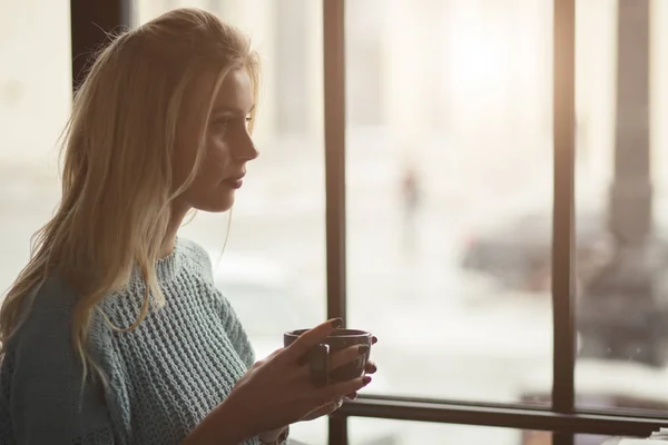 ผู้หญิงในชุด pullover นั่งกับถ้วยกาแฟในคาเฟ่ — ภาพถ่ายสต็อก