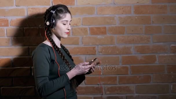 Mujer en auriculares escuchar música en la pared de ladrillo en habitación oscura — Vídeos de Stock