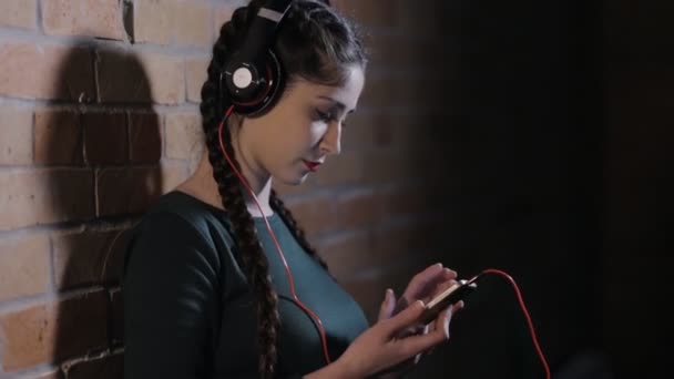 Женщина в наушниках слушает музыку у кирпичной стены в темной комнате — стоковое видео