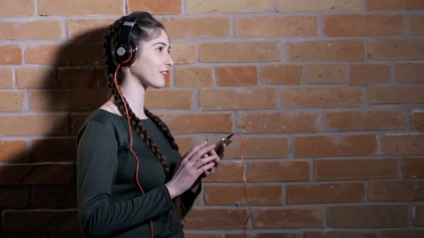 Mujer en auriculares escuchar música en la pared de ladrillo en habitación oscura — Vídeos de Stock