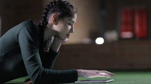 Женщина, использующая планшетный компьютер, лежит на полу ночью — стоковое видео