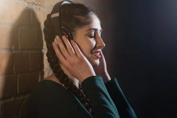 Mujer en auriculares escuchar música en la pared de ladrillo en habitación oscura —  Fotos de Stock
