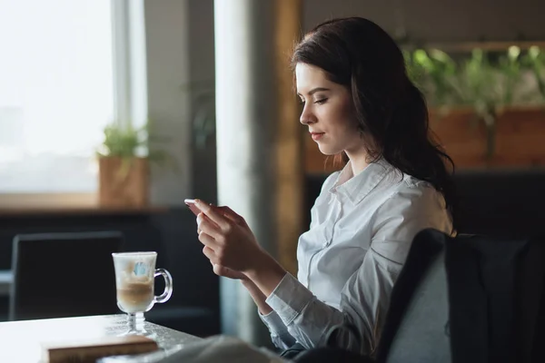 Business woman reading news on smart phone using app drinking latte in cafe
