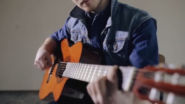 Чоловічий гітарист, який грає на акустичній гітарі, сидить на сірому фоні стіни — стокове відео