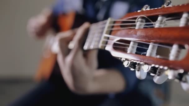 Крупним планом гітарист грає на акустичній гітарі, сидячи на сірому фоні стіни — стокове відео