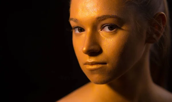 Professional model posing with bronze art makeup on her face closeup