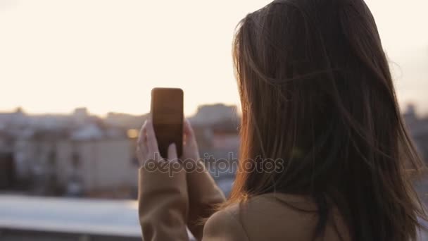 女被访者在日落时分拍摄她的智能手机对城市景观 — 图库视频影像