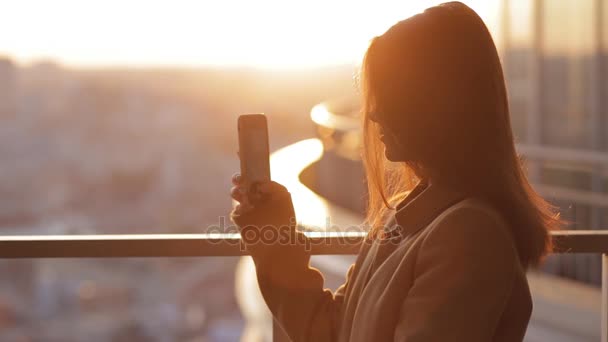 Mladá žena fotografování města na západ slunce z mrakodrapu — Stock video