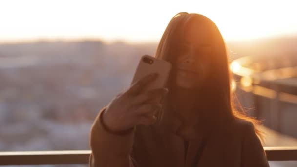 Ung kvinna gör en selfie på skyskrapa i sunset city — Stockvideo