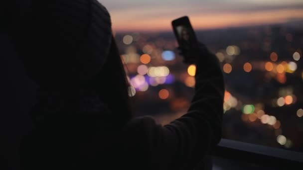 Kobieta fotografowania wieczorem panoramę miasta z wysokiego wieżowca. Lampki nocne miasto. — Wideo stockowe