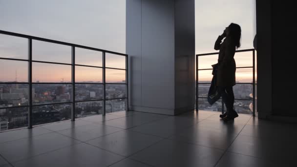 Σιλουέτα του νεαρή γυναίκα σε υψηλό ουρανοξύστης μιλώντας από το smartphone, το βράδυ — Αρχείο Βίντεο