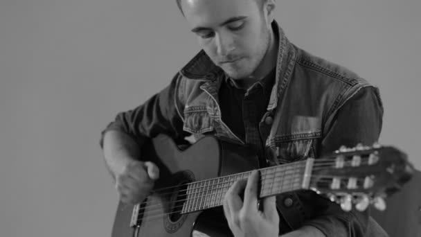 Gitarzysta gra na gitarze akustycznej, siedział przy ścianie szary tło - monochromatyczne — Wideo stockowe